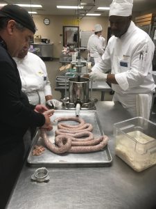 Photo of Chef Geybrayel, left, demonstrating part of the sausage making process as Stacey Dillard and Simon Stanley look on. The sausages will be featured at the college’s upcoming Grand Buffet on Aug. 2.