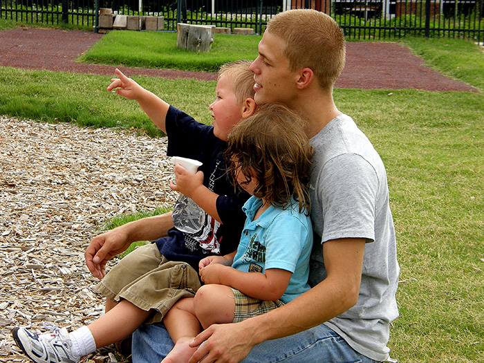 Male Early Childhood instructor sitting on grass with two children