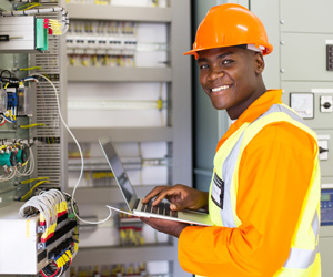 A man in a hardhat working on wires in an open panel