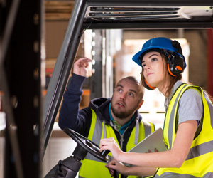 A man and woman wearing hardhats in a forklift