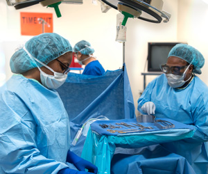 Surgical technology students dressed in surgical attire choosing medical instruments as they practice on a mannequin