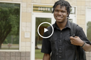 Smiling male Dual Achievement student carrying a backpack with campus building in background