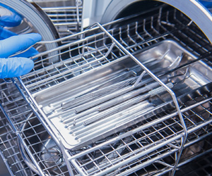 Gloved hand placing a tray of dental instruments into a sterilization chamber.